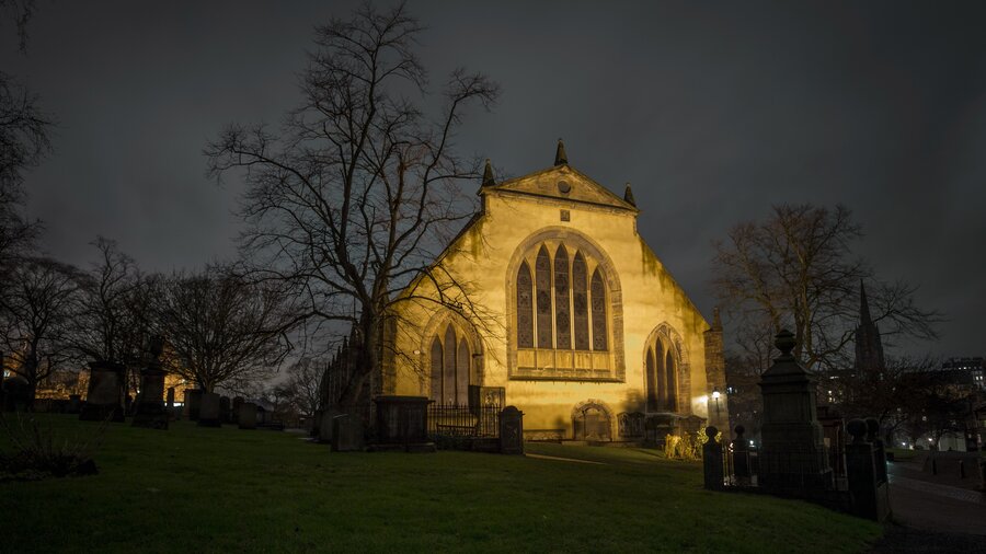 Greyfriar's Kirk, Edinburgh - A lit up building with stained glass windows with bare trees on either side, at night. (© Visit Scotland)